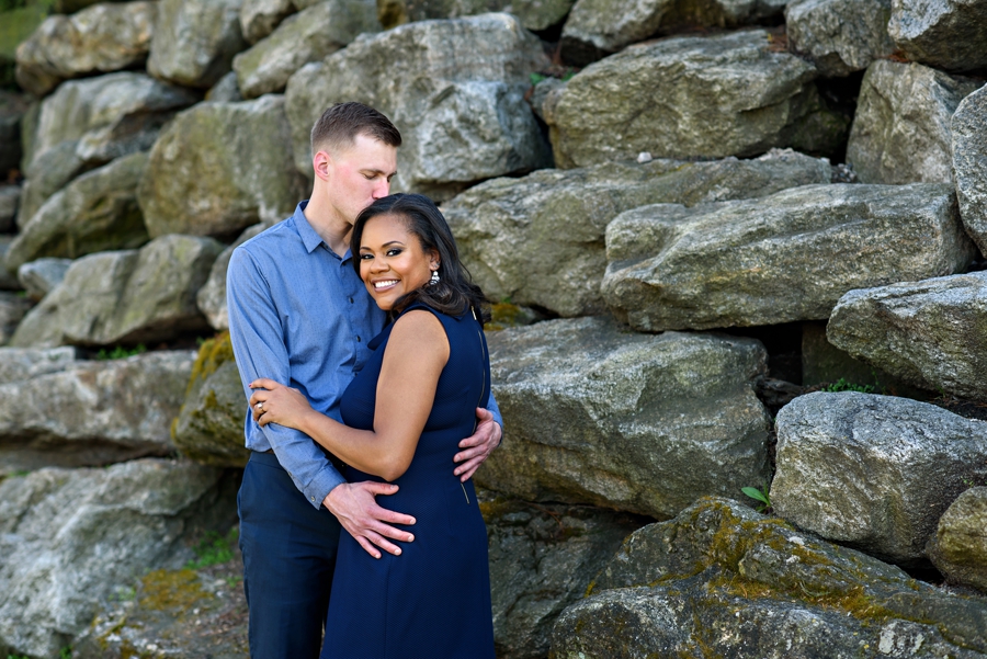 A beautiful couple embrace in front of the rocks on the side of The Art Museum of Philadelphia.